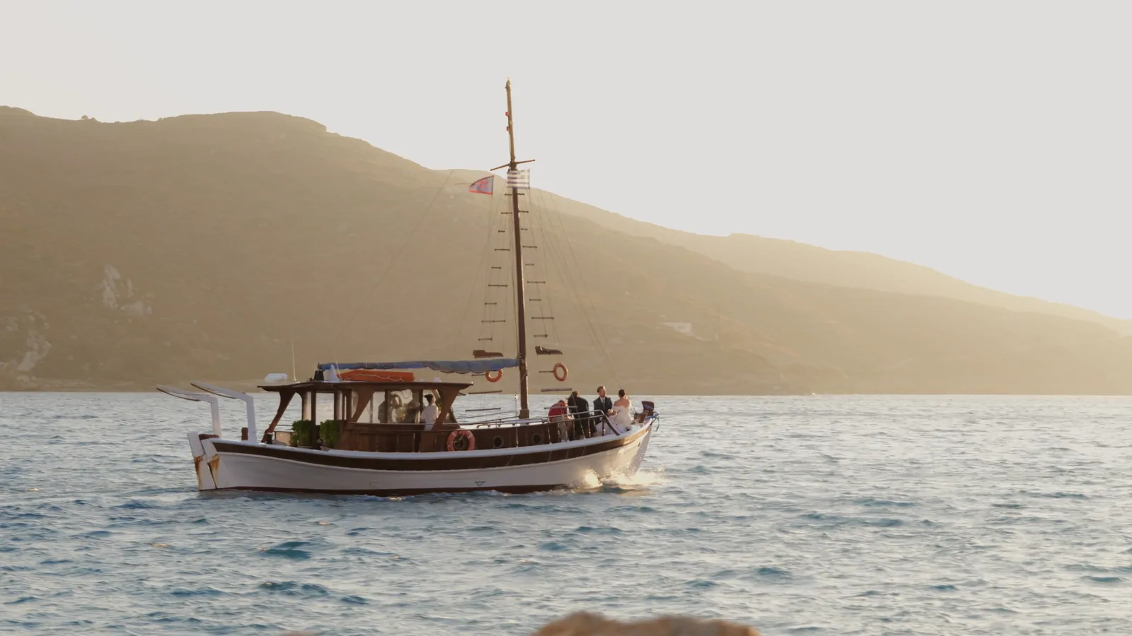 Barca in legno al tramonto davanti a una collina, ripresa da riva